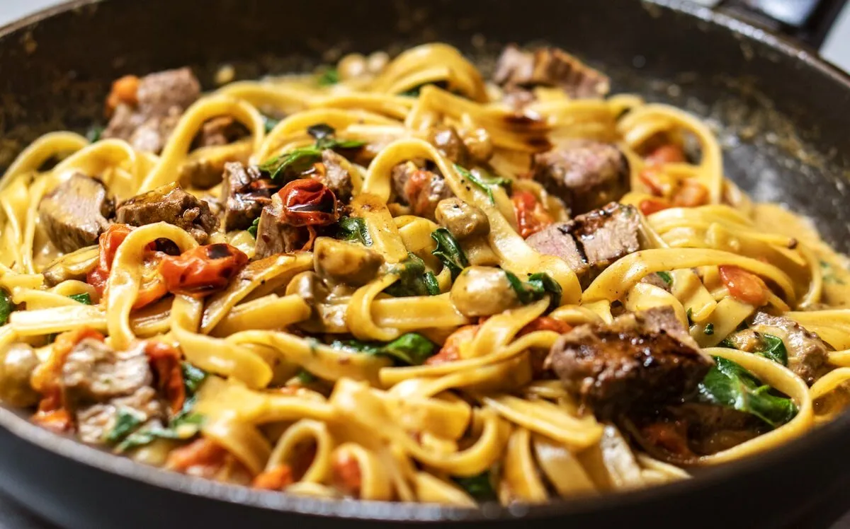 Frische Pasta mit Sauce, Tomaten und Kräutern in der Pfanne